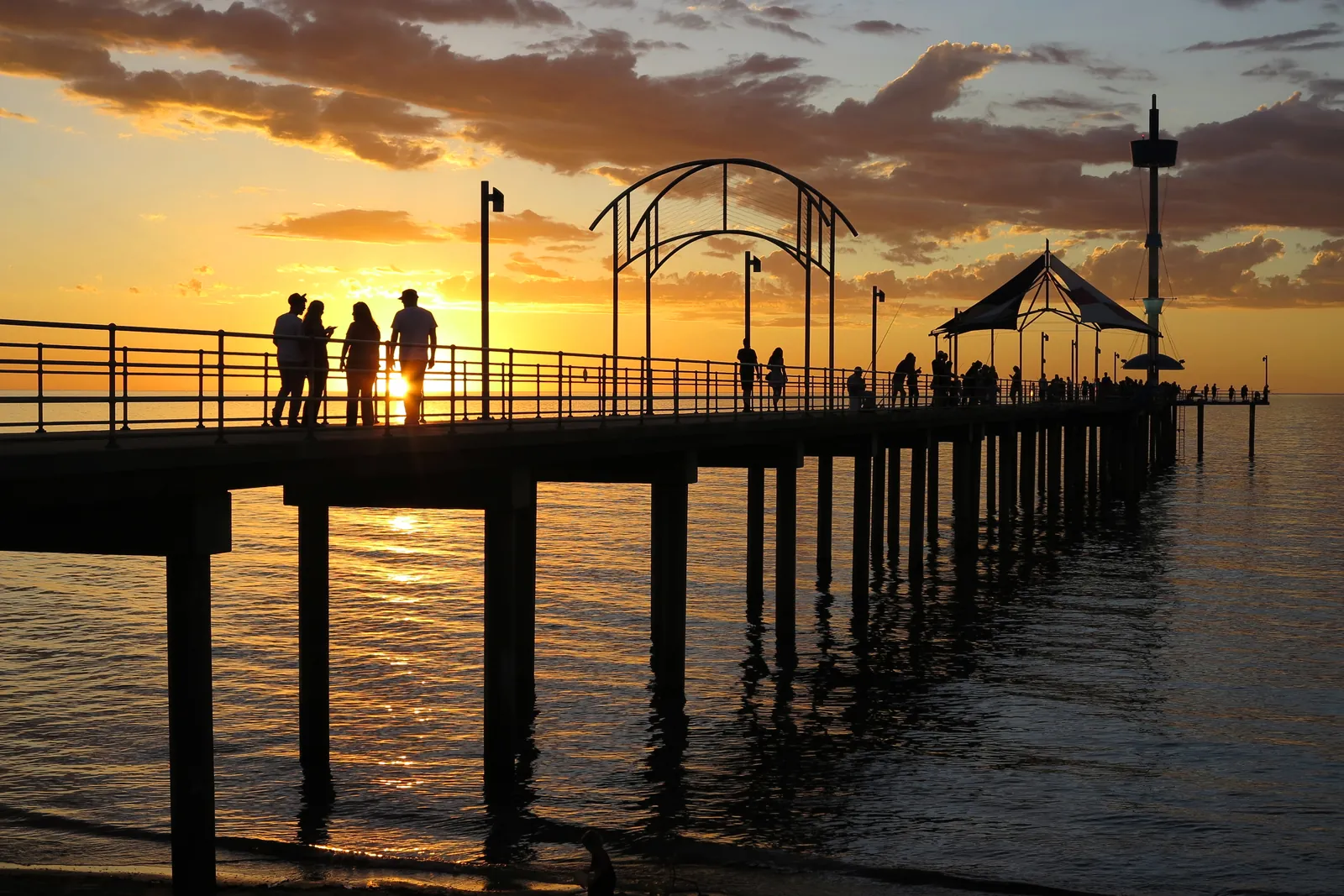 People silhouetted on Brighton Jetty at sunset, with an orange sky over the sea