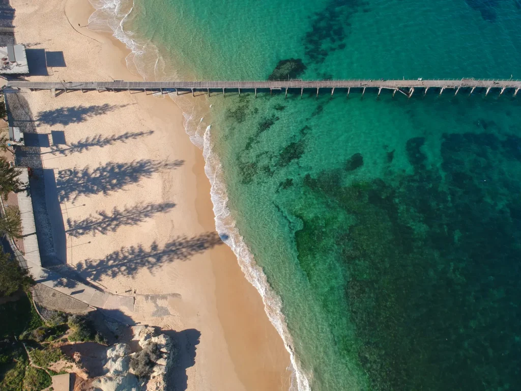 Aerial view of Port Noarlunga Jetty over clear turquoise water and a sandy beach